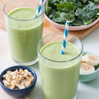 Two kale smoothies in glasses with straws.