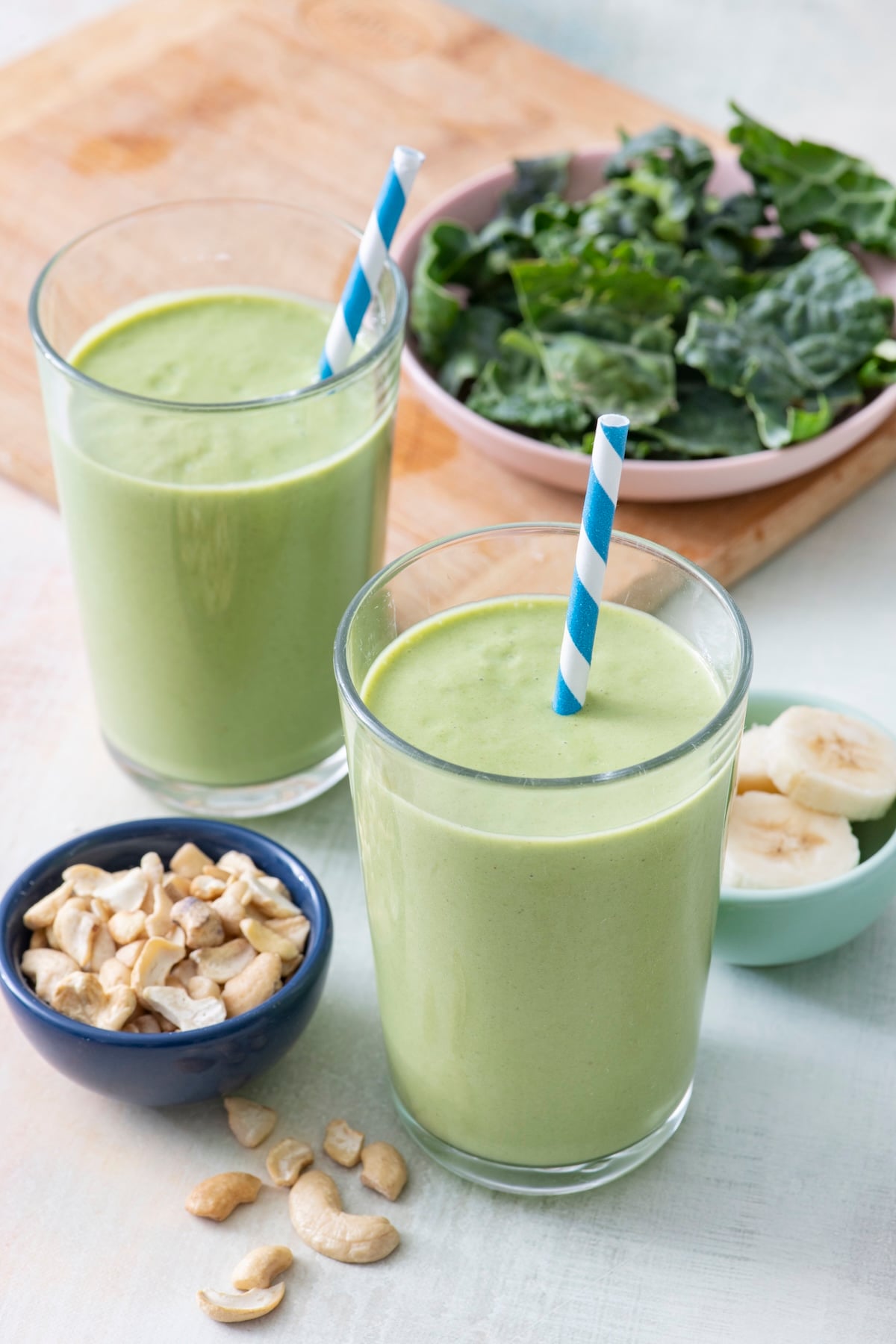 Two kale smoothies in glasses with straws.