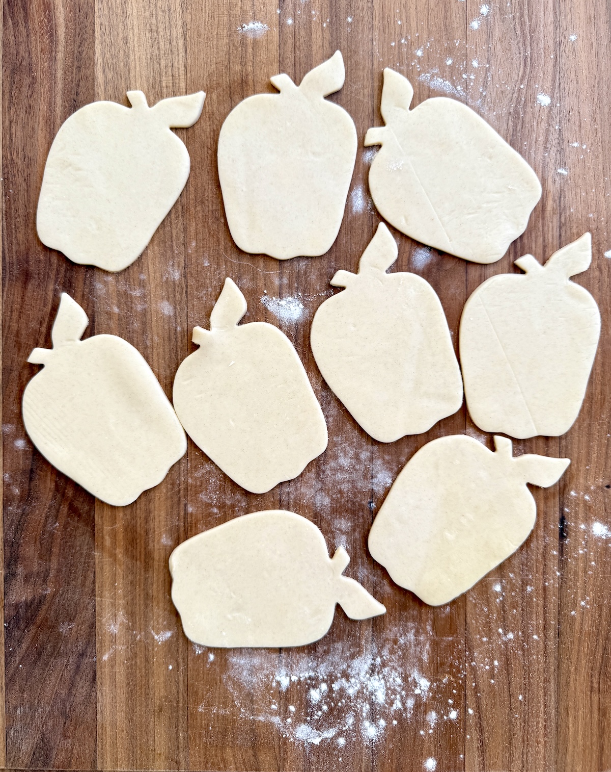 Apple shaped pie dough cutouts on a wooden surface.
