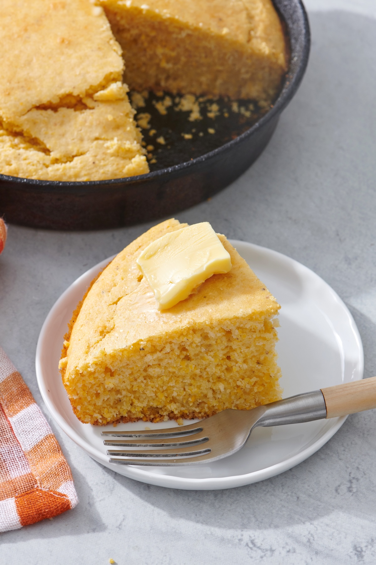 A slice of cornbread with a pat of butter on a plate.
