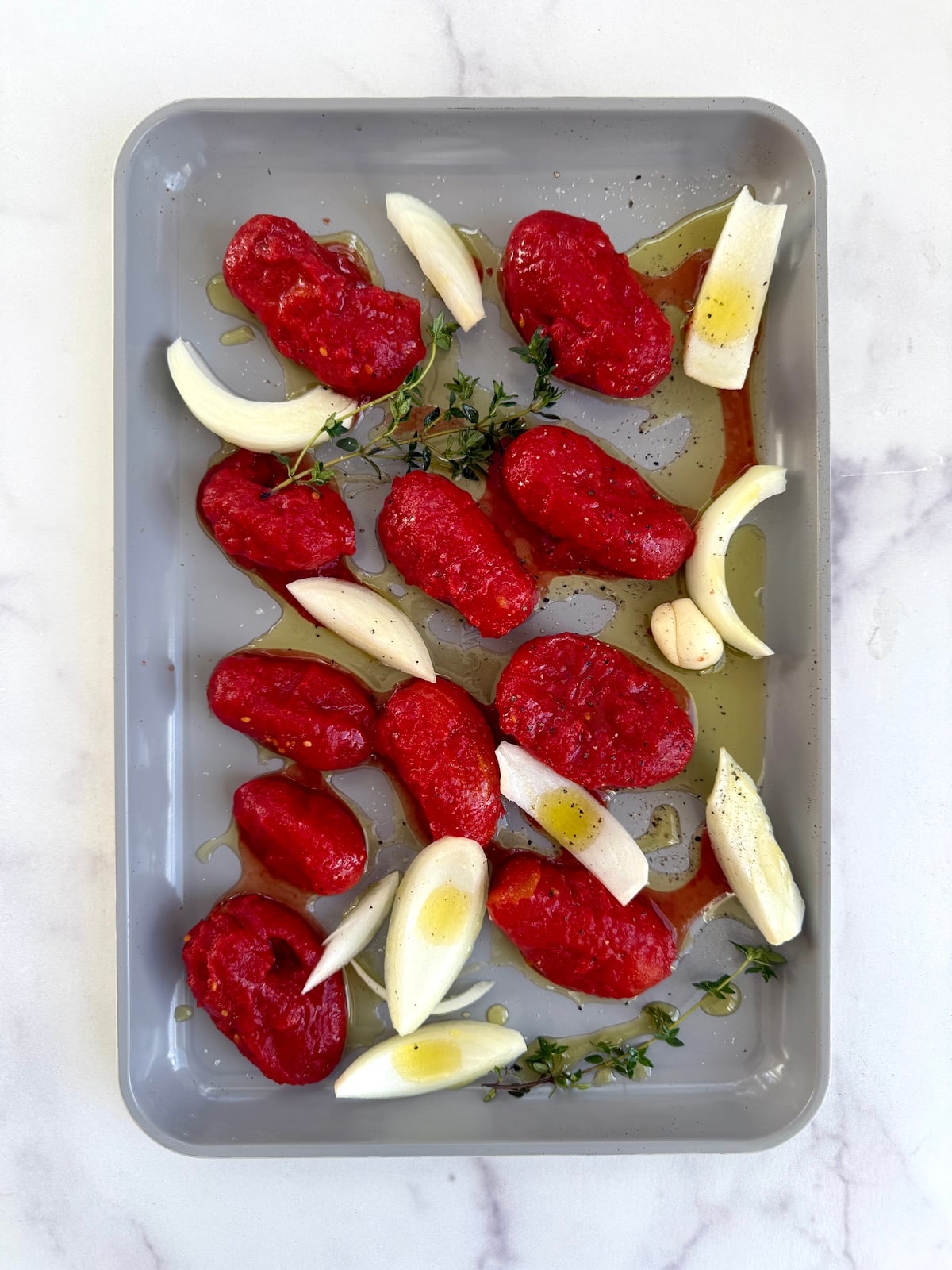 Tomatoes, onion and thyme tossed in olive oil on a sheet pan.