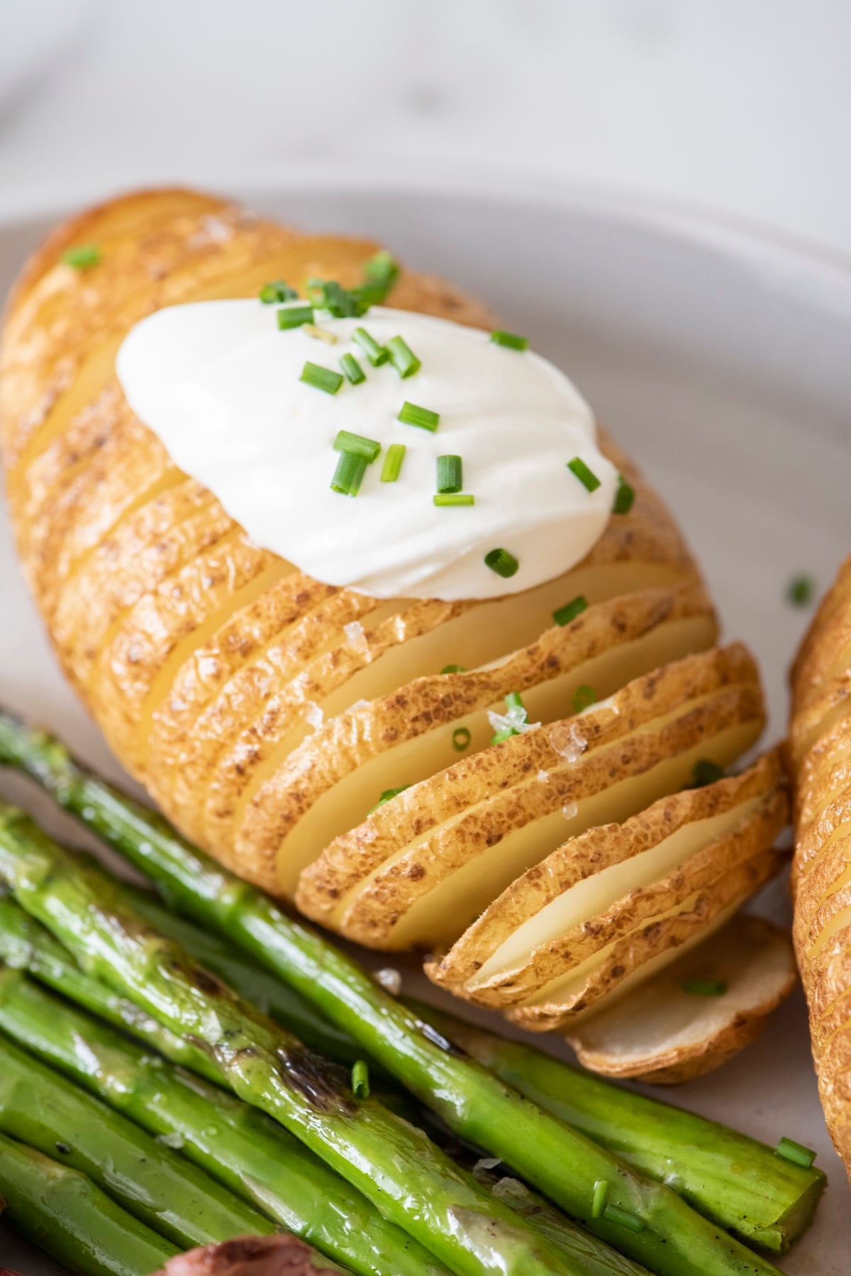 Hassleback potato on a plate topped with sour cream and chives.