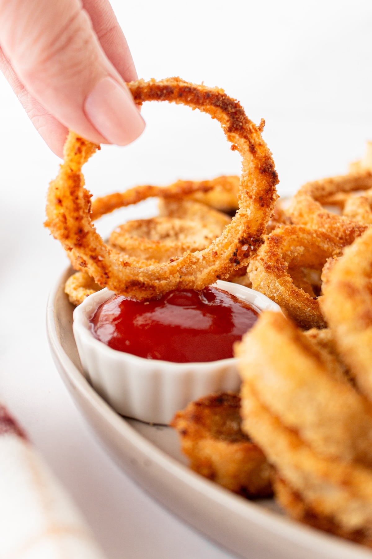 A hand dippings an onion ring in ketchup.