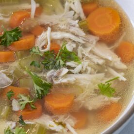 A bowl of pressure cooker chicken soup with carrots and topped with parsley.