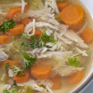 A bowl of pressure cooker chicken soup with carrots and topped with parsley.