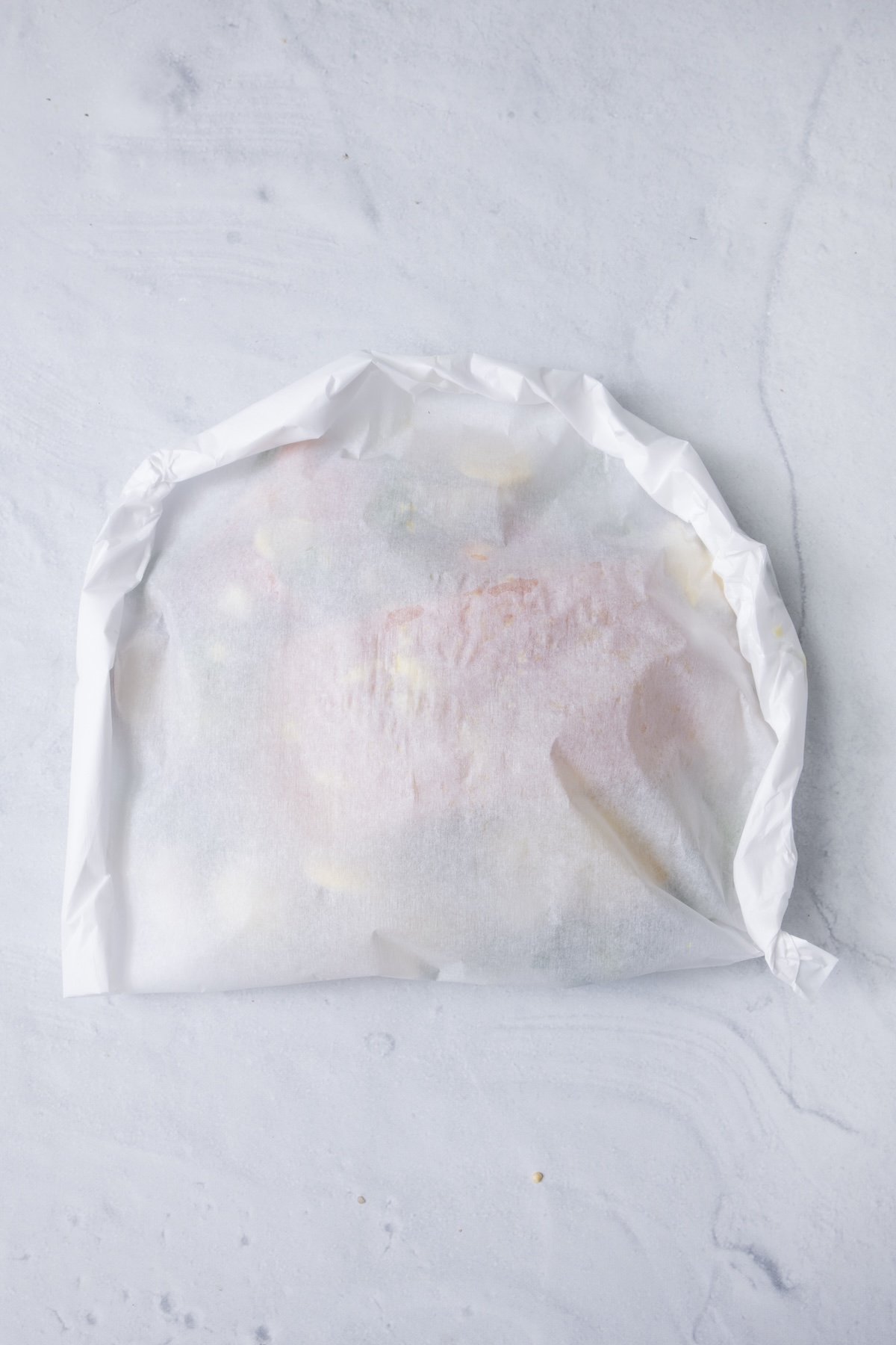 A single sealed fish en papillote packet on a white marble surface, ready to bake.