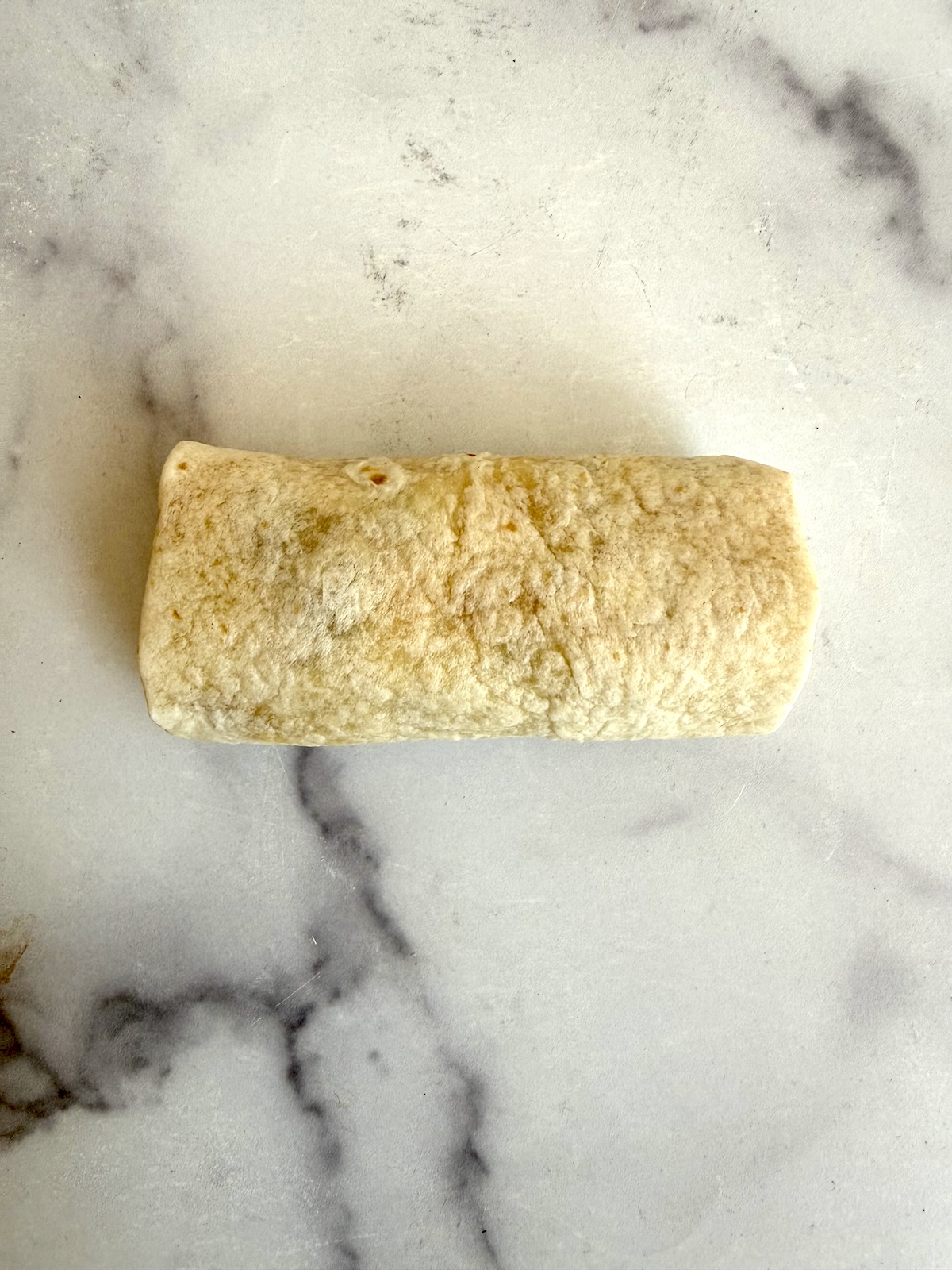 A rolled up burrito ready to toast in a skillet.