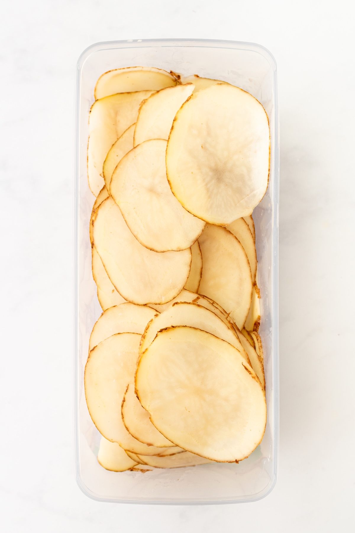 Thinly sliced potatoes in a container.