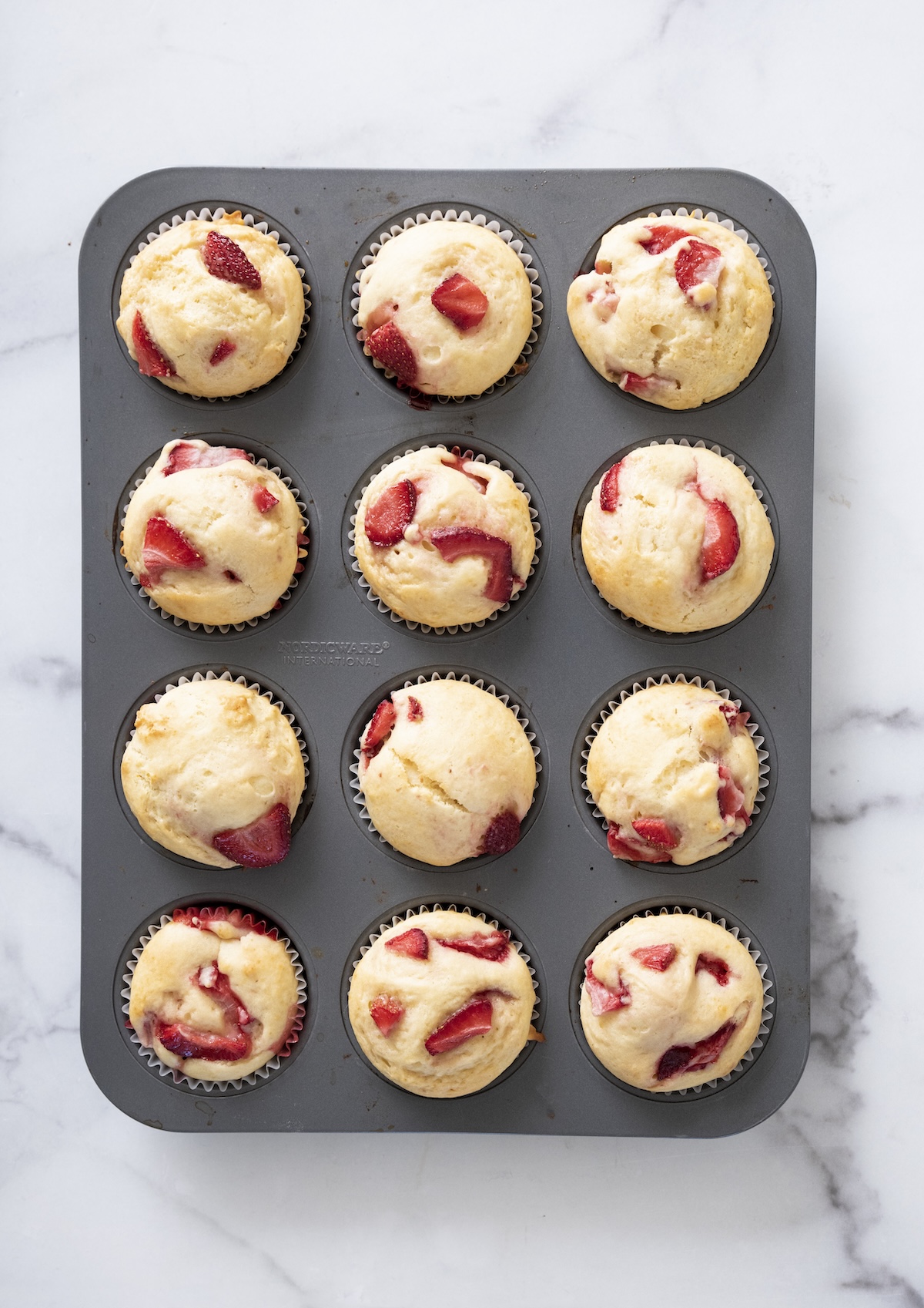 A pan of freshly baked strawberry muffins golden and risen.
