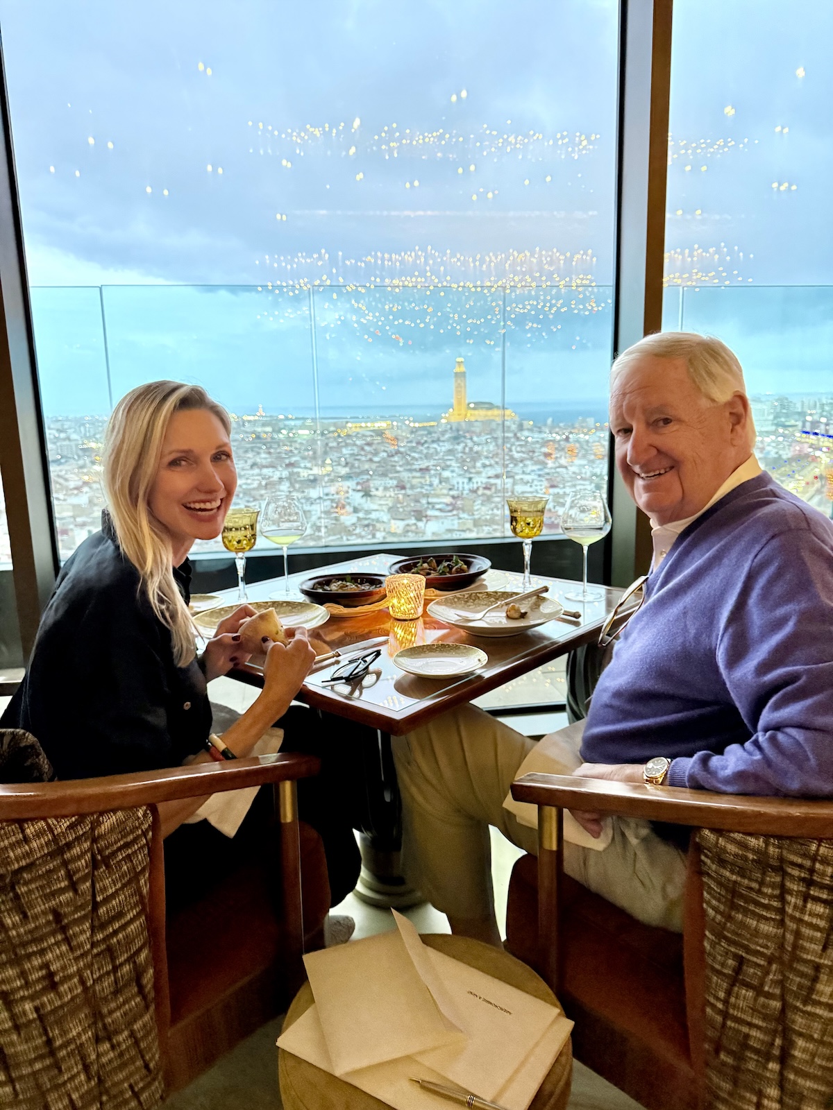 Catherine and her dad dining at La Grande Table Marocaine, with the Hassan II Mosque lit up against the Casablanca skyline through the floor-to-ceiling windows.