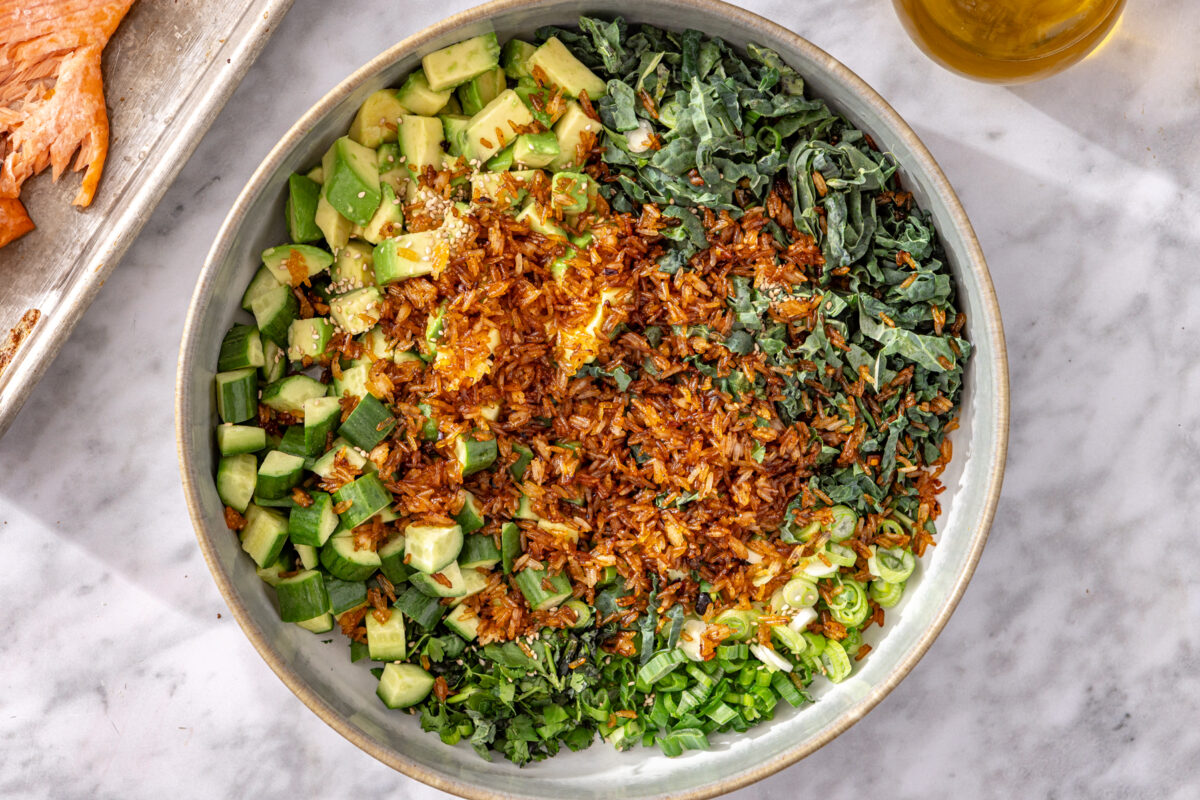 Golden crispy chili crisp rice added to salad bowl with kale, avocado, and cucumber.