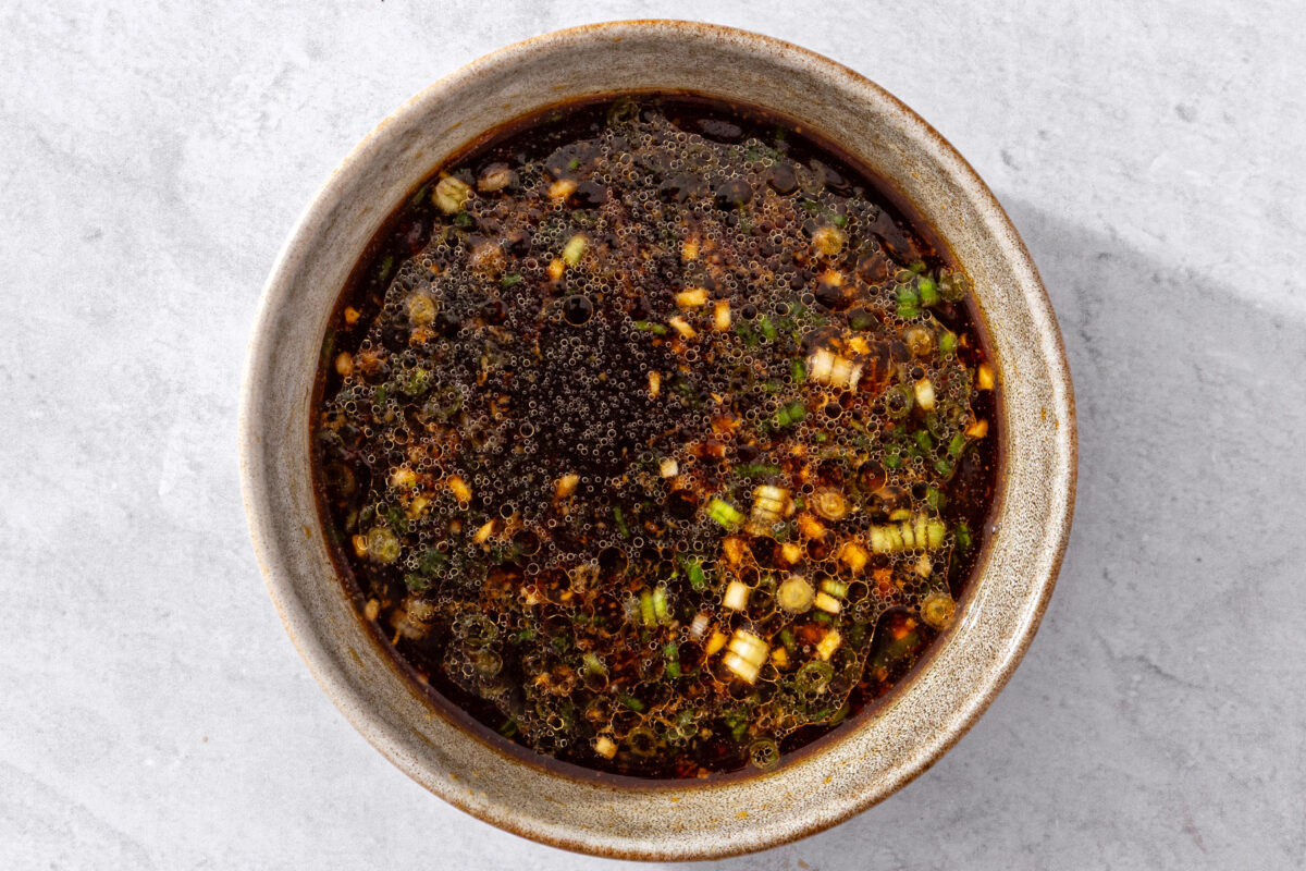 Dumpling dipping sauce with soy sauce, sesame oil, scallions, and ginger in a bowl.