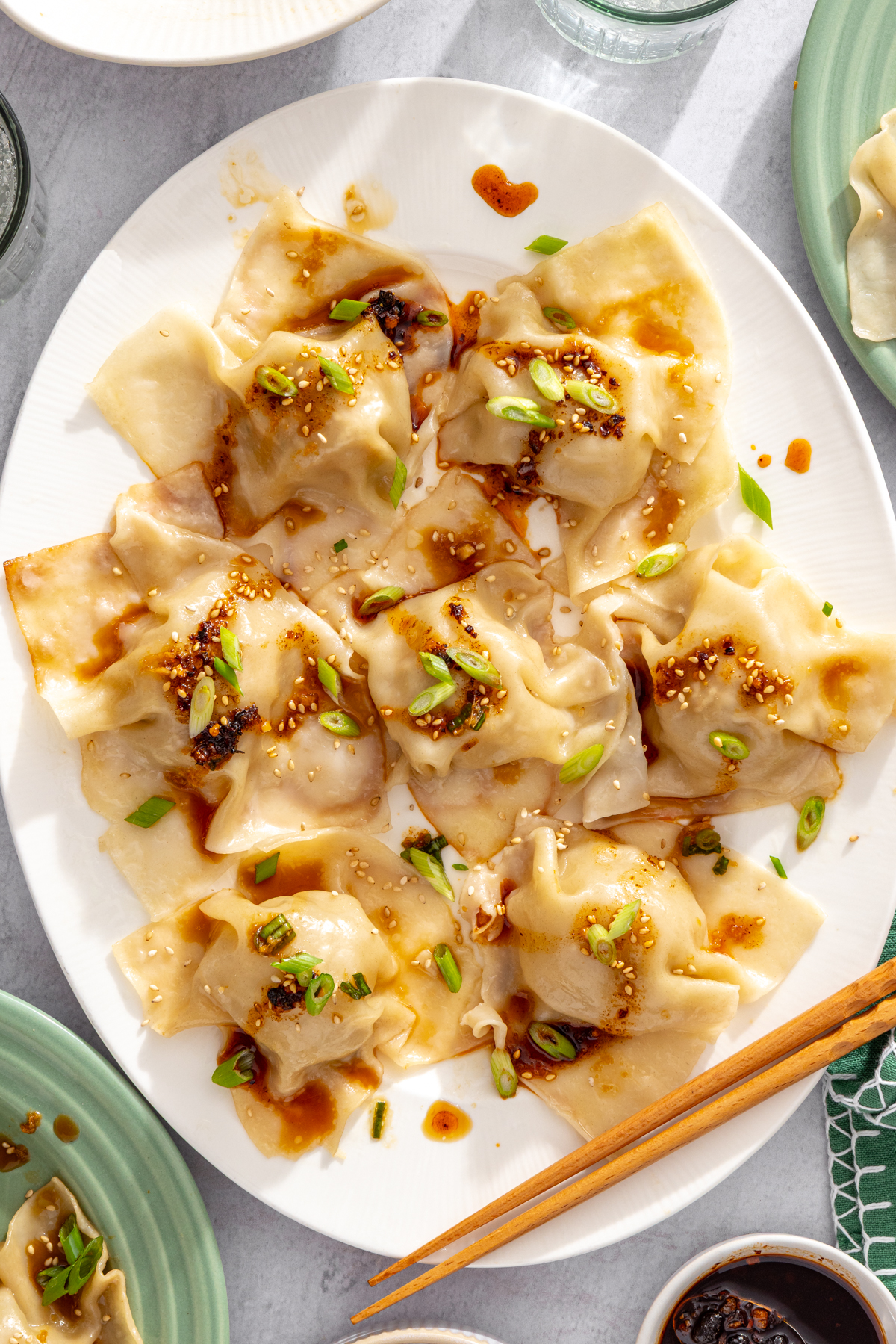 A platter of blanket dumplings drizzled with dipping sauce, sesame seeds, and scallions.