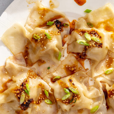 Overhead close-up of blanket dumplings with sesame seeds, scallions, and chili oil.