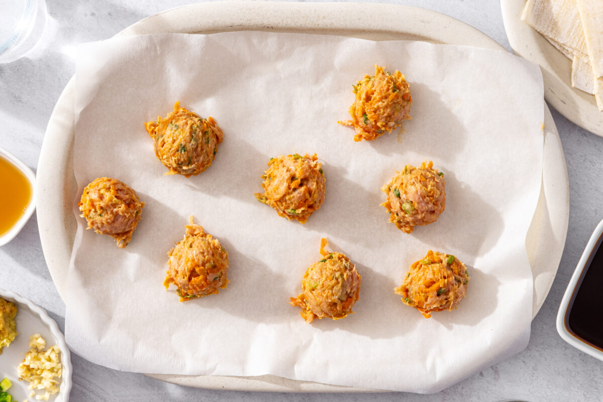 Eight seasoned ground meat meatballs spaced on a parchment-lined plate.